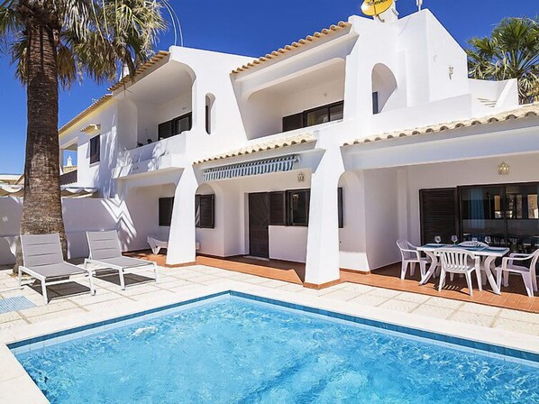 A two-story building with a swimming pool, white walls, and a tiled roof.