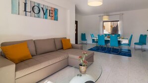 Una sala de estar moderna con un sofá color crema, una zona de comedor con sillas azules y una obra de arte grande con la palabra 'LOVE'.