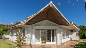 Une maison de plain-pied avec un toit en pente, un porche à l’avant doté de portes vitrées et une terrasse dallée.
