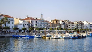 Un port de plaisance où sont amarrés des bateaux, entouré d’immeubles à plusieurs étages dotés de balcons, sous un ciel dégagé.