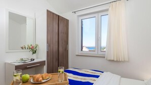 A hotel room with a bed, a bedside table with a tray of breakfast, a window with curtains, and a view of the sea.
