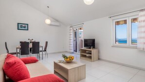 A modern living room with a sofa, coffee table, TV, dining area, and a view of the sea.