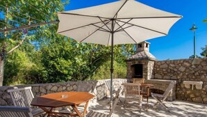 An outdoor patio with a stone wall, a wooden table, and chairs.
