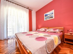 A bedroom with a bed, a nightstand, a painting, and a window with curtains.