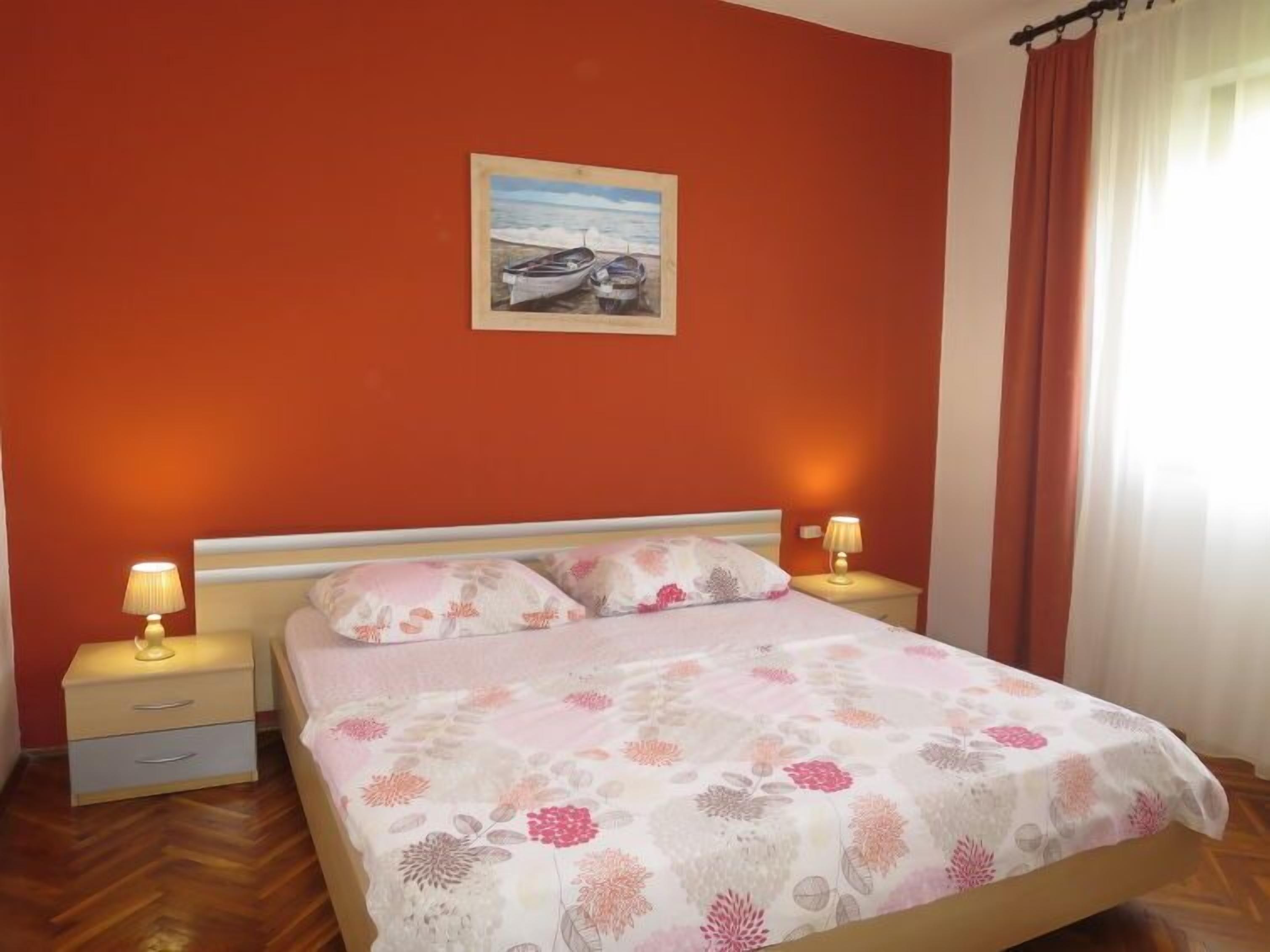 Ein Schlafzimmer mit einem Bett, zwei Nachttischen, einem Wandbild und einem Fenster mit Vorhängen.