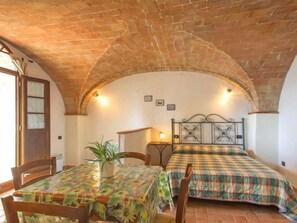 A room with a brick ceiling, a bed with a plaid bedspread, a table with a floral tablecloth, and a potted plant.