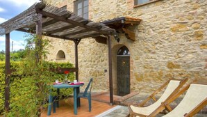 Un edificio in pietra con una pergola, un tavolo con sedie e due poltrone da relax.