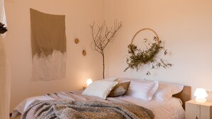 A neatly made bed with a blanket, two bedside lamps, a wall-mounted plant, and a piece of abstract art. - Villa Griota by Interhome (Umag)