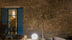 A room with a stone wall, a wooden chair, a table, and a small tree. - Villa Griota by Interhome (Umag)