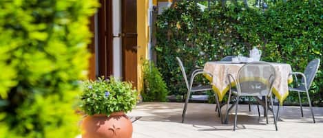 A patio with a table and chairs, a potted plant, and a yellow building in the background.