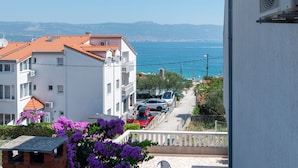 Ein Küstenwohngebiet mit weißen Gebäuden, freiem Blick auf das Meer und einer gepflasterten Straße mit parkenden Autos.