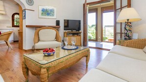 Un salon comprenant une table basse en osier, un canapé, un téléviseur et un coin repas avec des meubles en osier.