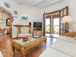 Un salon comprenant une table basse en osier, un canapé, un téléviseur et un coin repas avec des meubles en osier.