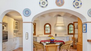 Une cuisine avec des meubles blancs, une table à manger entourée de chaises en osier et des assiettes décoratives accrochées au mur.