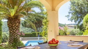 Un espace extérieur aménagé pour les repas, avec une table dressée pour quatre personnes, entouré de verdure et bordé d’une piscine.