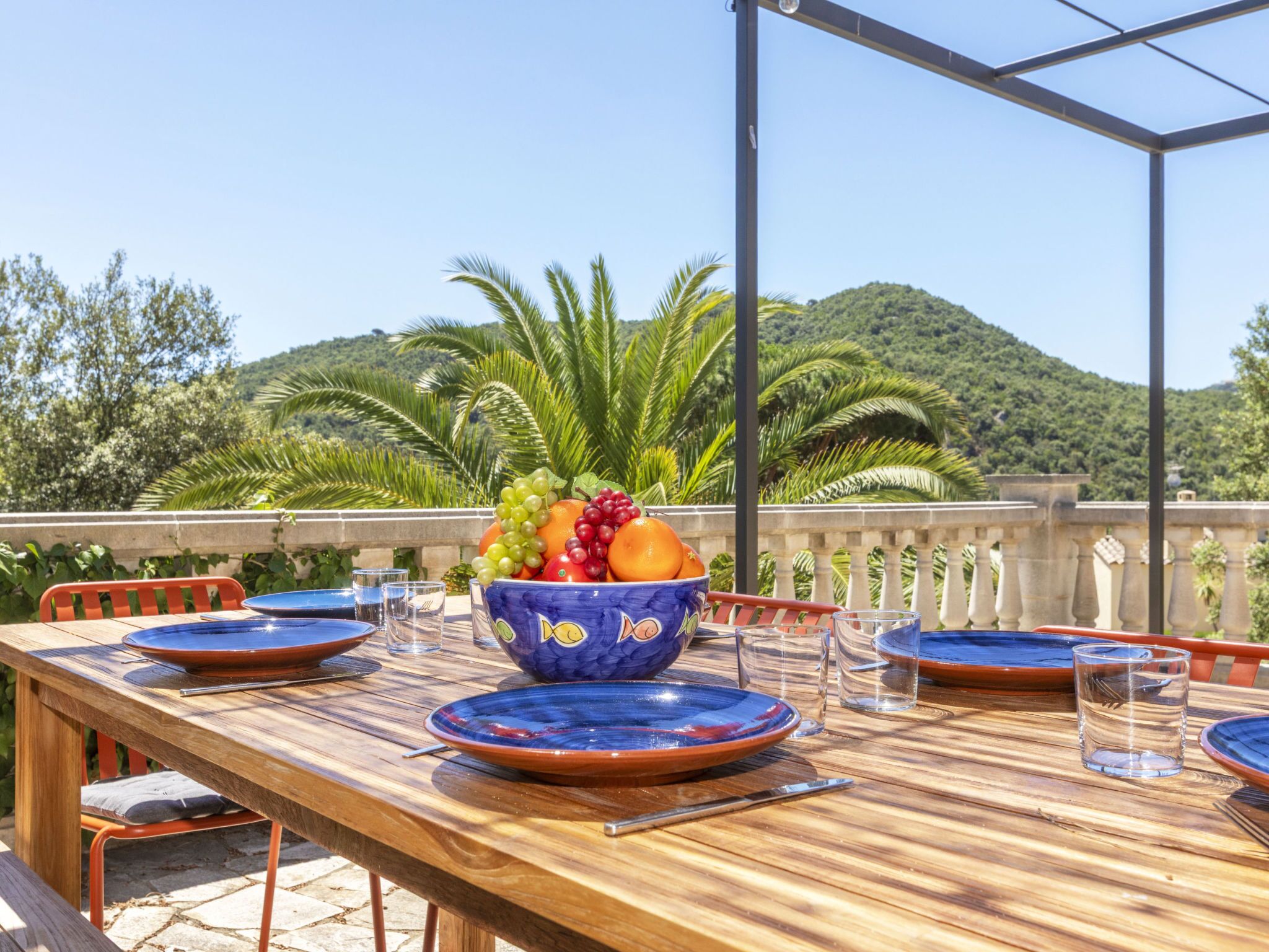 Un espace extérieur aménagé pour les repas, avec une table en bois, des chaises et un panier de fruits.