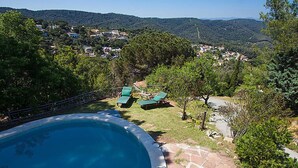 Une piscine dotée d’une terrasse en bois et de chaises longues, entourée de verdure et avec des collines en arrière-plan.