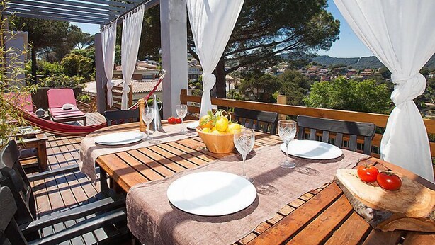 Un espace de restauration en plein air avec des tables et des chaises en bois, des nappes blanches et une vue sur le paysage.