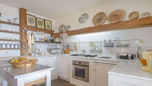 A kitchen with white cabinets, a wooden beam ceiling, and various kitchen utensils hanging on the wall. - Paradiso by Interhome (Perugia)