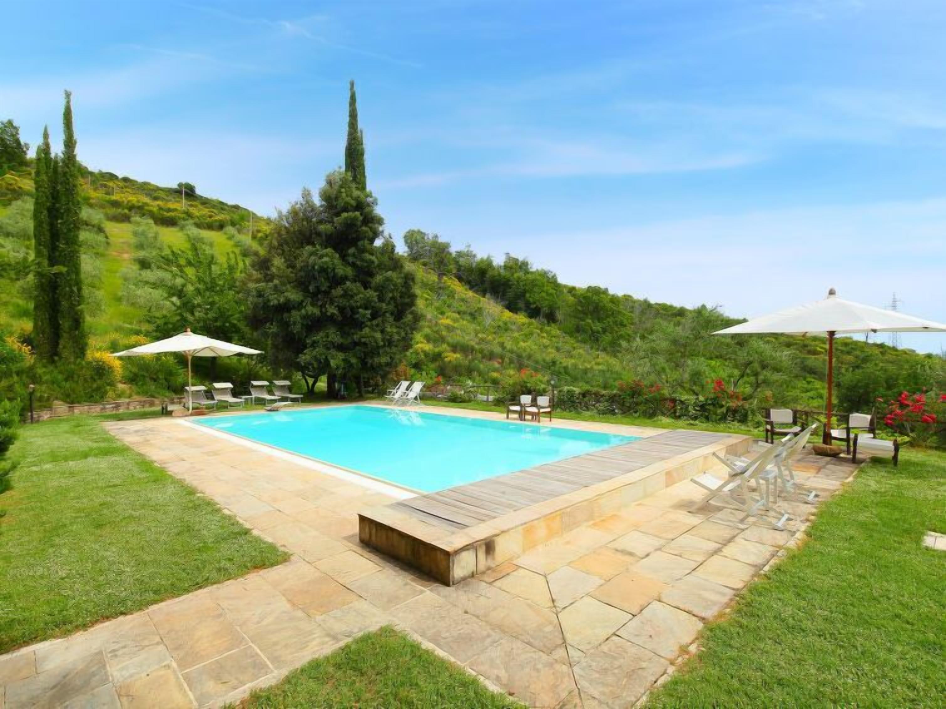A rectangular swimming pool with a stone deck, surrounded by grass and trees.