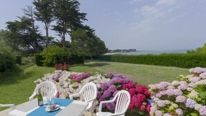 Un patio al aire libre con una mesa y sillas, rodeado de flores coloridas y vistas al mar.