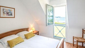 Un dormitorio con cama, mesita de noche, silla y un ventanal con vistas a la playa.