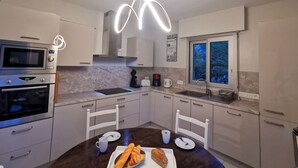 A modern kitchen with a built-in microwave, oven, and a dining area with a table set for two. - Les Rimains by Interhome (Cancale)