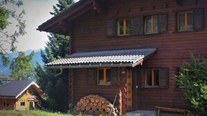 A wooden cabin with a tiled porch, a stack of firewood, and a bench outside. - L'Alpage by Interhome (Ovronnaz)