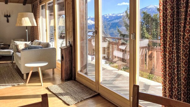 A cozy living room with a sofa, a small table, and a lamp. Large windows offer a view of a snowy mountain landscape. - L'Alpage by Interhome (Ovronnaz)