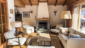 A cozy living room with a stone fireplace, wooden beams, and a large window offering a view. - L'Alpage by Interhome (Ovronnaz)