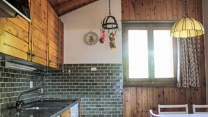 A kitchen with wooden cabinets, a brick backsplash, a sink, and a dining area with a table and chairs. - L'Alpage by Interhome (Ovronnaz)