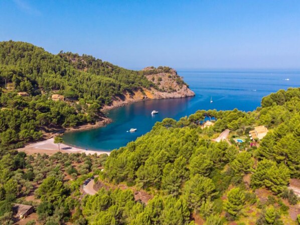 A coastal landscape with dense greenery, a small rocky island, and boats on the water.