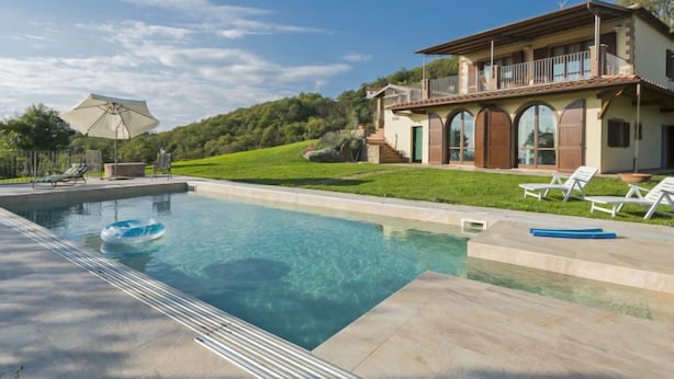 Una piscina grande con zona de estar y una casa con balcón.