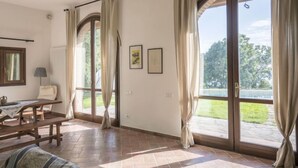 Amplia habitación con un gran ventanal corredera que da a un balcón, una mesa de madera y una silla.