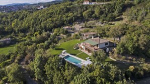 Una villa en la ladera con piscina, rodeada de exuberante vegetación y vistas al pueblo lejano.