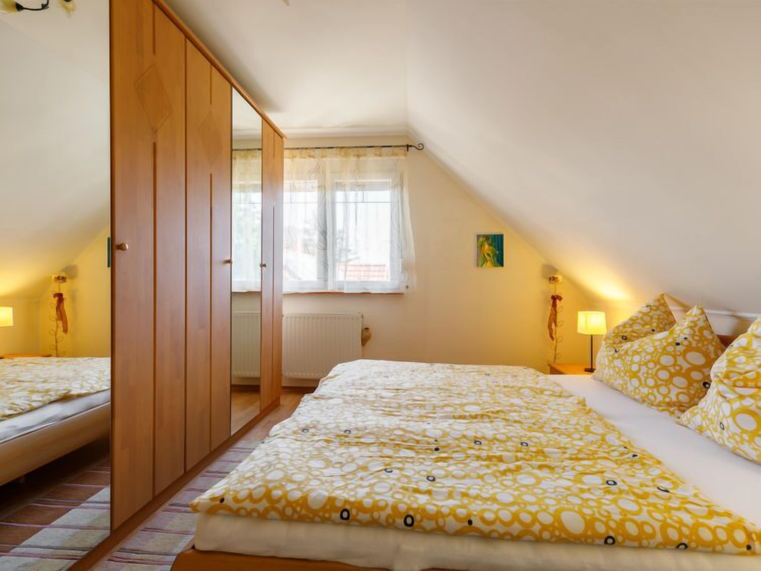 A bedroom with a bed, a wardrobe, a window with curtains, and a bedside lamp.