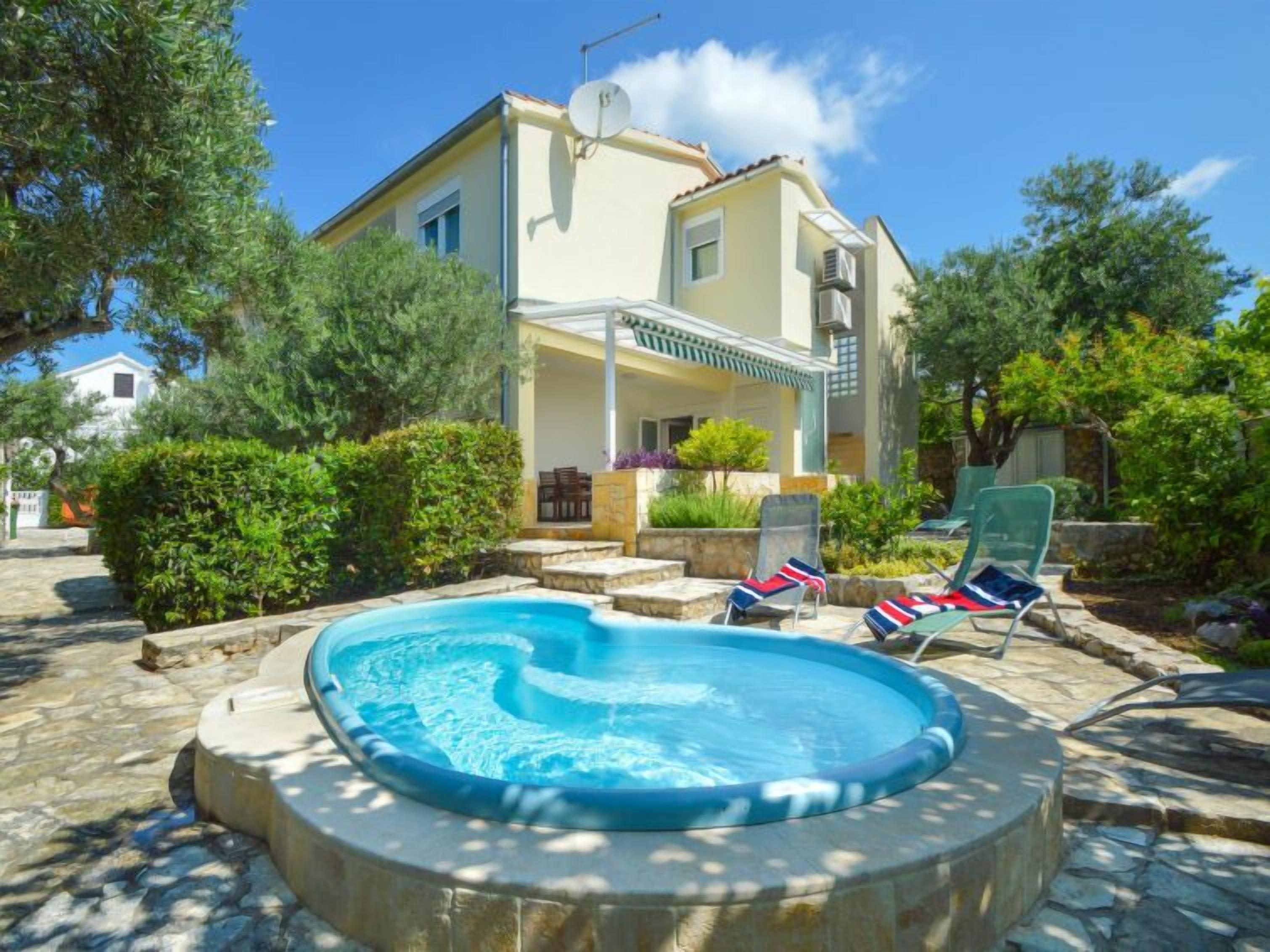 A pool area with a hot tub, lounge chairs, and a building with a covered patio.