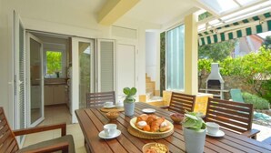 Ein Holztisch ist mit Speisen und Getränken gedeckt, eine Terrasse mit Stühlen und Blick ins Grüne.