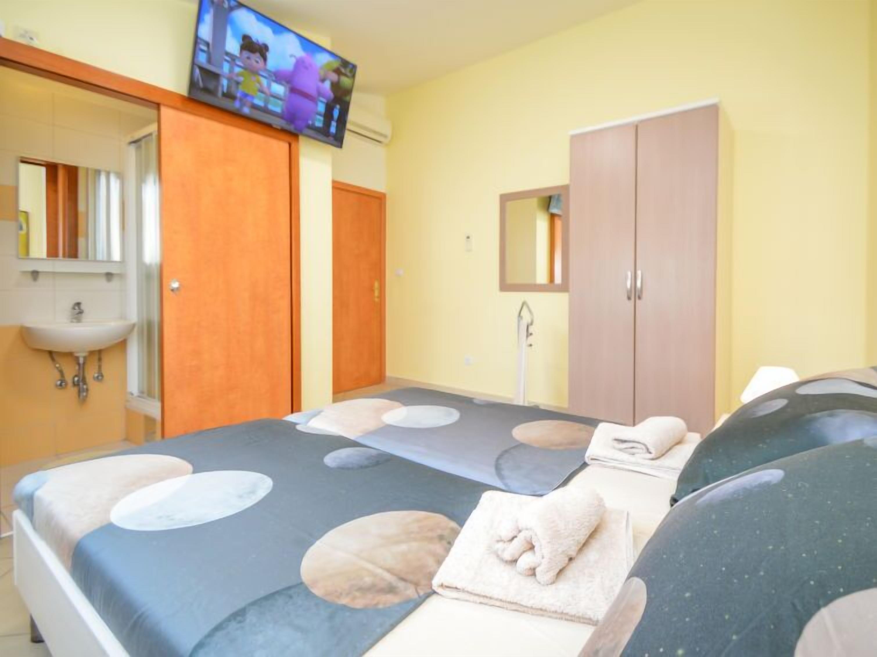 Hotellihuone, jossa on sänky, seinälle asennettu televisio, vaatekaappi ja pesuallas.