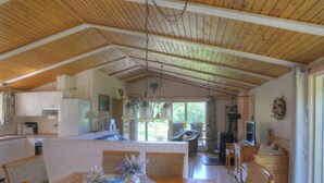 Une cuisine spacieuse avec des poutres en bois, un coin repas avec des chaises en osier et un salon avec un canapé et une télévision.