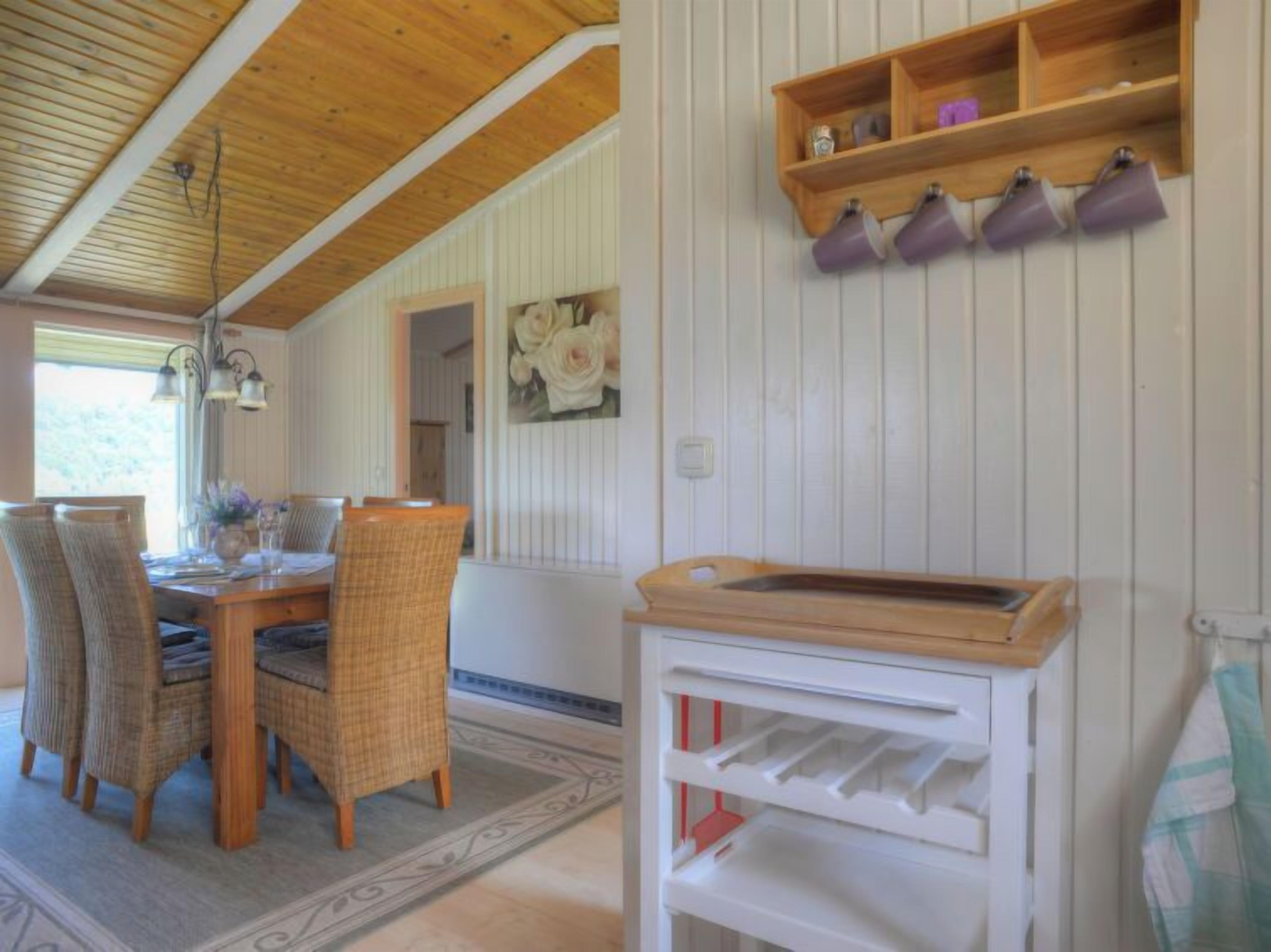 Ein Essbereich mit Holztisch und Korbstühlen, einem weißen Schrank mit Regalen und einer Holzbalkendecke.