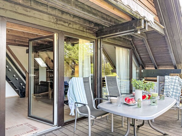 Un espace extérieur abrité, aménagé avec une table, des chaises et offrant une vue sur l’intérieur.