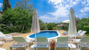 A swimming pool with lounge chairs and umbrellas, surrounded by greenery and trees. - Apartment Mariza by Interhome (Labin)