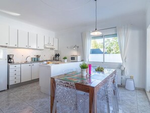 Una cocina moderna con armarios blancos, una mesa de comedor con sillas, un ventanal con cortinas y una lámpara colgante.