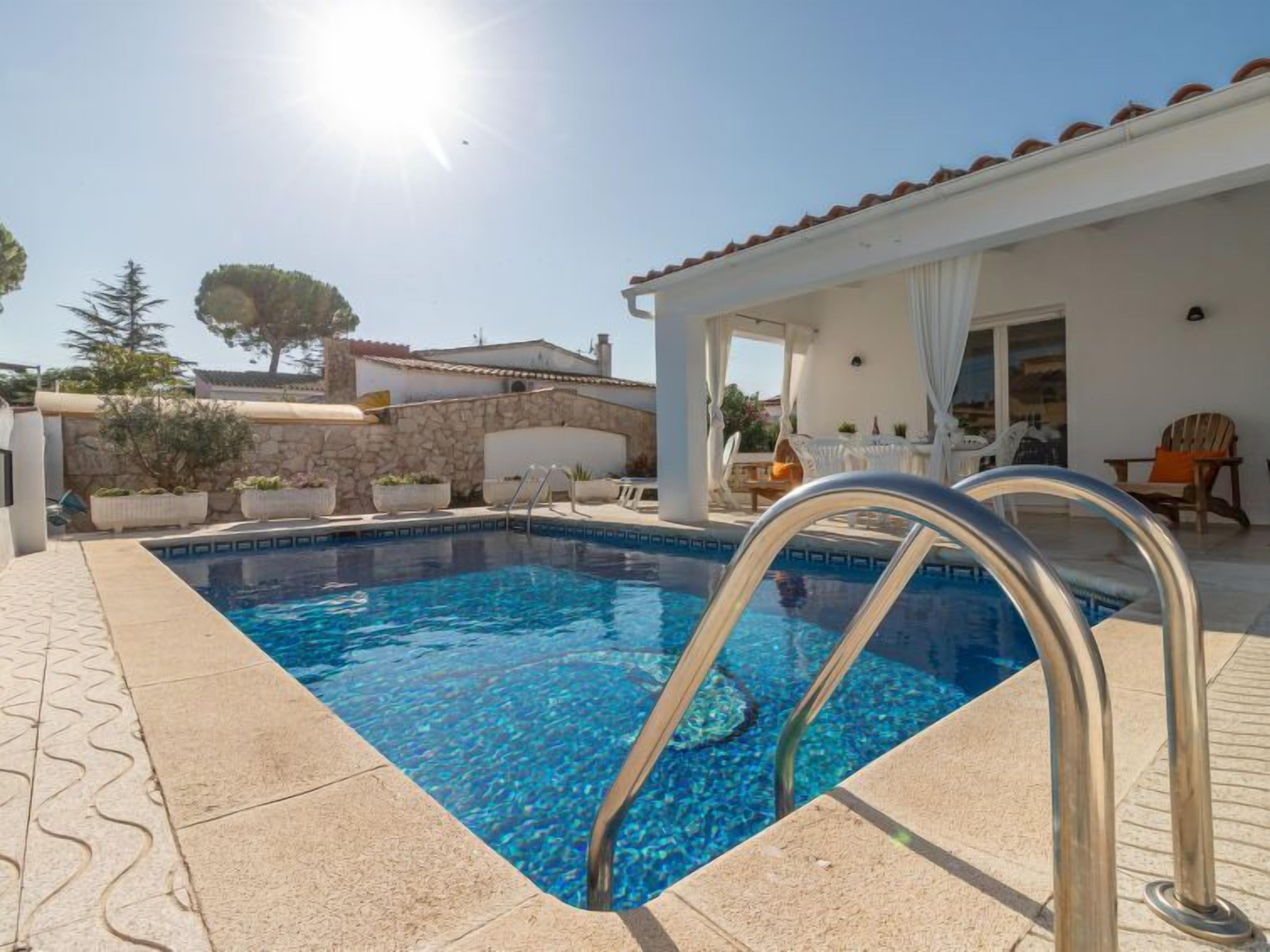 A swimming pool with a metal ladder, surrounded by a stone wall and potted plants.