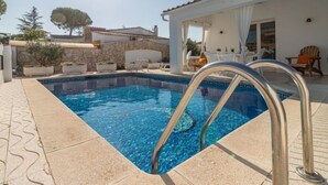 Una piscina con una escalera metálica, rodeada por un muro de piedra y plantas en macetas.