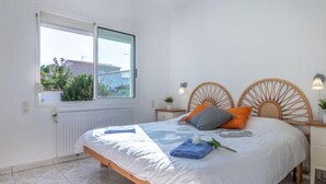 Un dormitorio con cama, ventana, radiador y mesita de noche con lámpara.