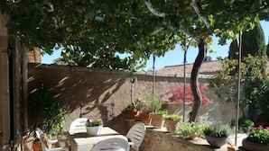 Una terrazza esterna con tavolo e sedie, circondata da piante in vaso e un muro in pietra.
