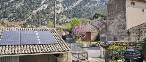 A rustic building with a tiled roof and solar panels, surrounded by a well-maintained garden and a mountainous backdrop.