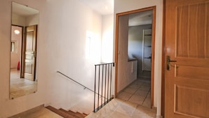 Una scala con corrimano, una porta in legno e un corridoio che conduce a una stanza con termosifone.